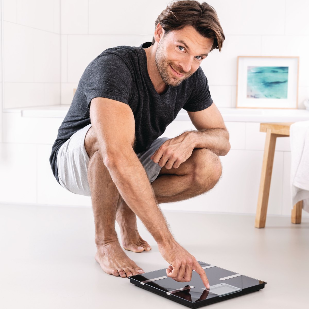 Man crouching to switch on a Beurer diagnostic bathroom scale