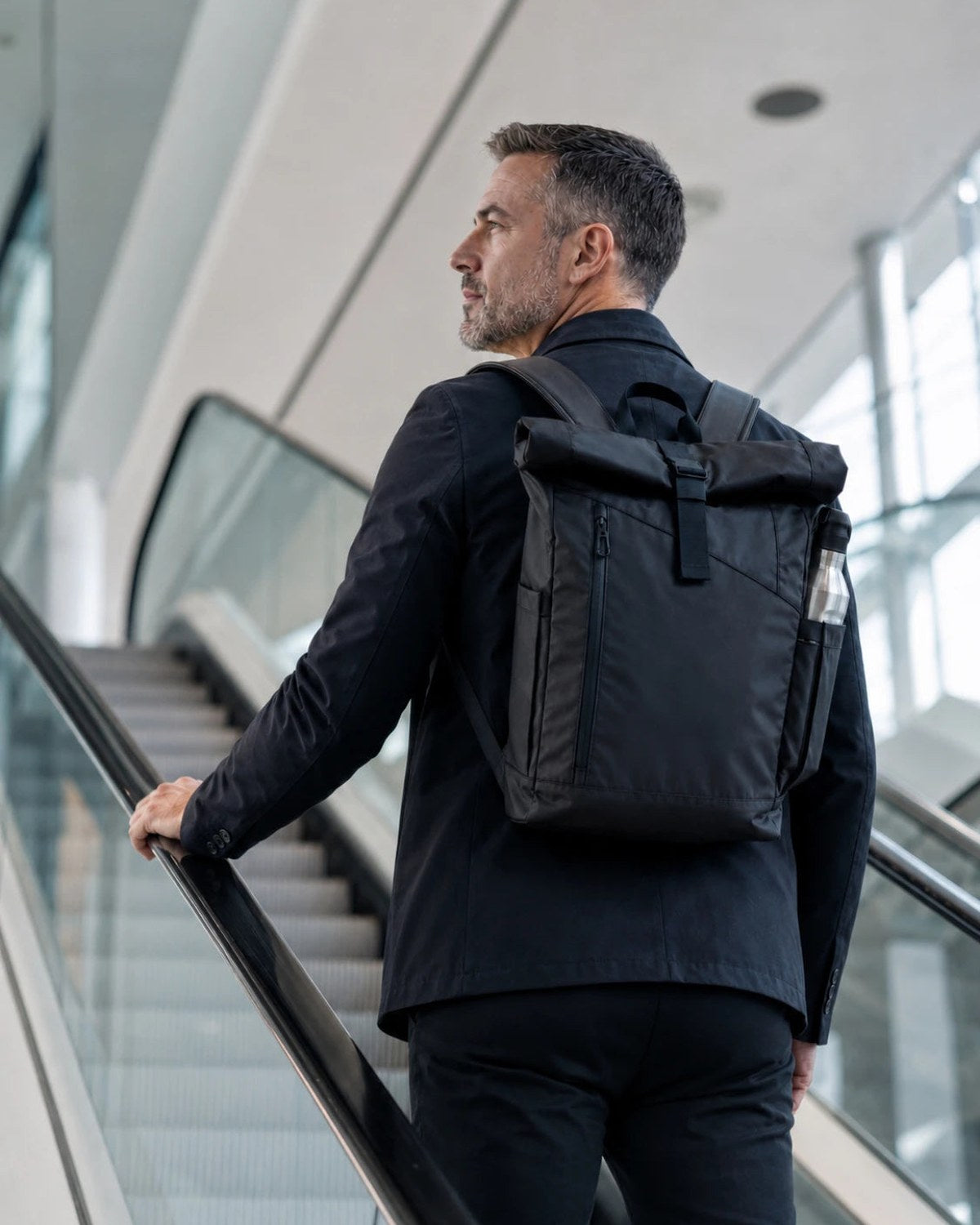 Man on an airport escalator with a TROIKA roll-top backpack