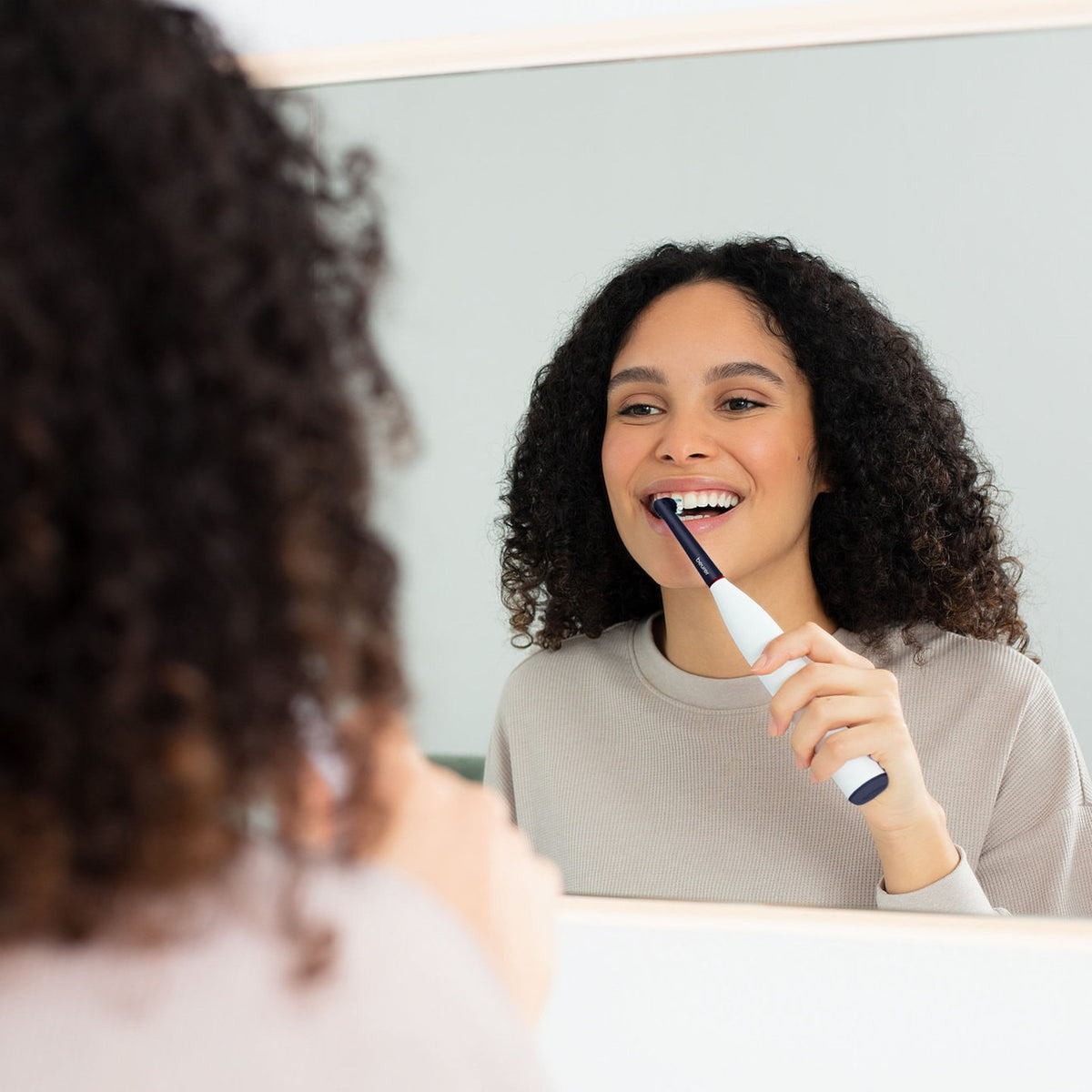 A woman brushing her teeth at the mirror with the Beurer TB 15