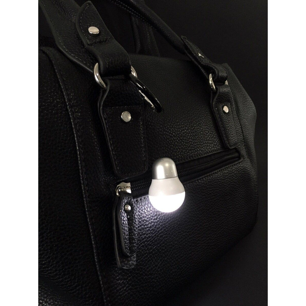 TROIKA silver light bulb bag light clipped to a black handbag, lit